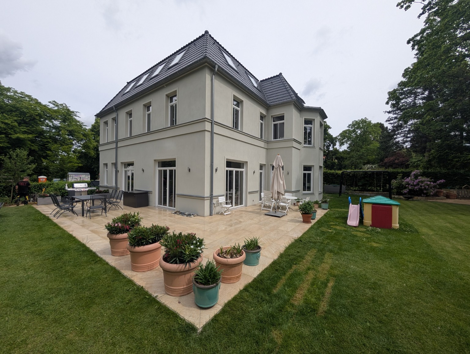 Terrasse rund um ein Wohnhaus mit Rasen und Pflanzgefäßen